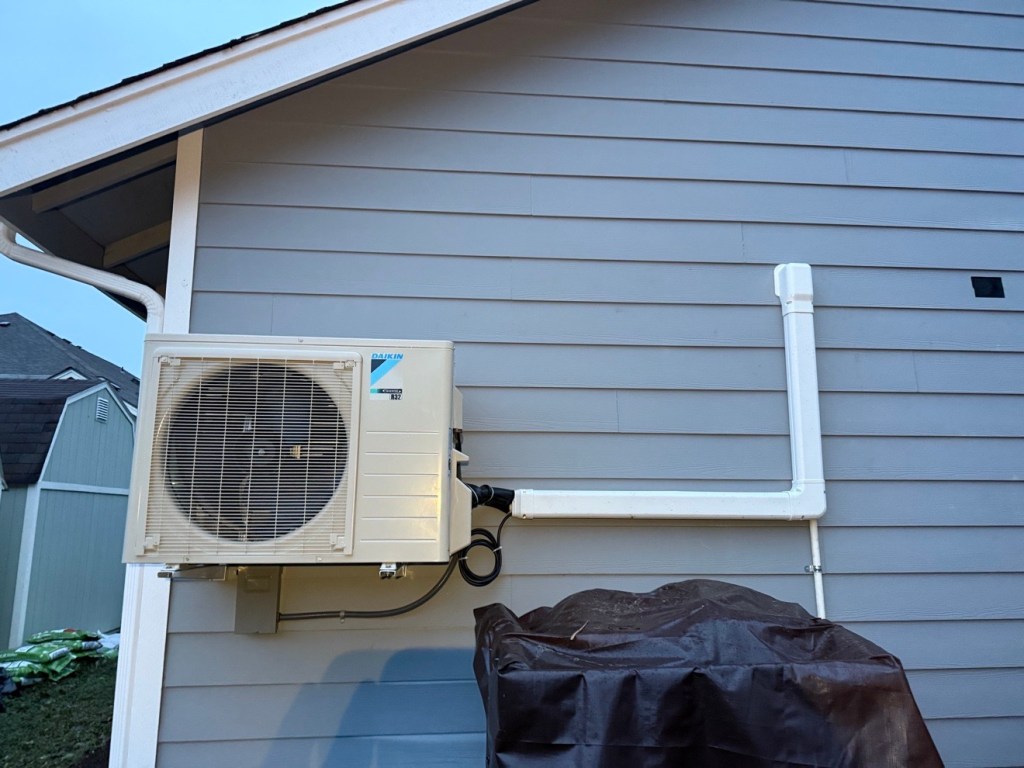 Mitsubishi Electric outdoor heat pump unit beside a shingle house